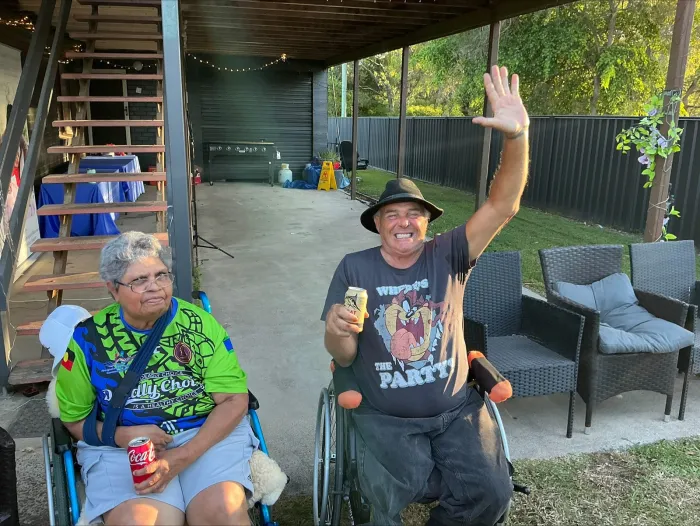 A participant and a support worker relaxing together under a carport