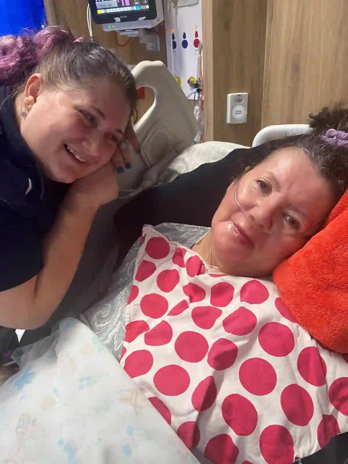 May smiling warmly in hospital care alongside one of her support workers